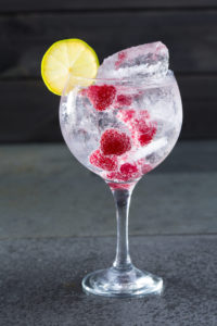 Gin tonic cocktail with raspberry lima slice and ice on black
