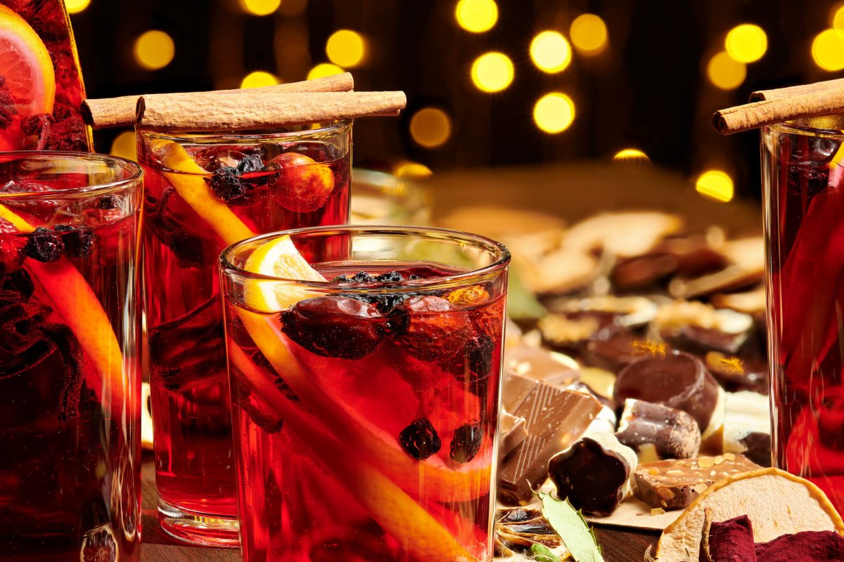 Christmas mulled wine or gluhwein with spices, chocolate sweets and orange slices on rustic table, traditional drink on winter holiday, christmas lights and decorations